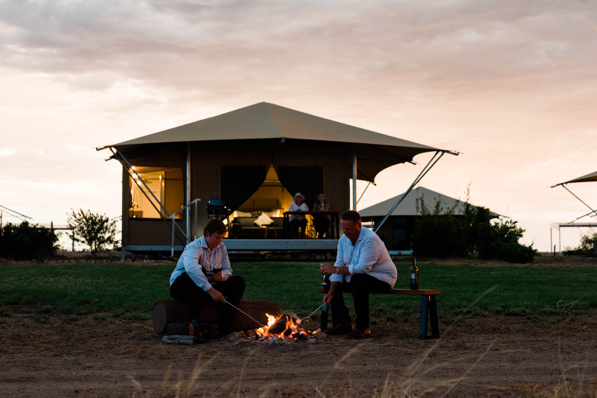 Private fire pit outside of glamping tent with father and son toasting marshmallows.