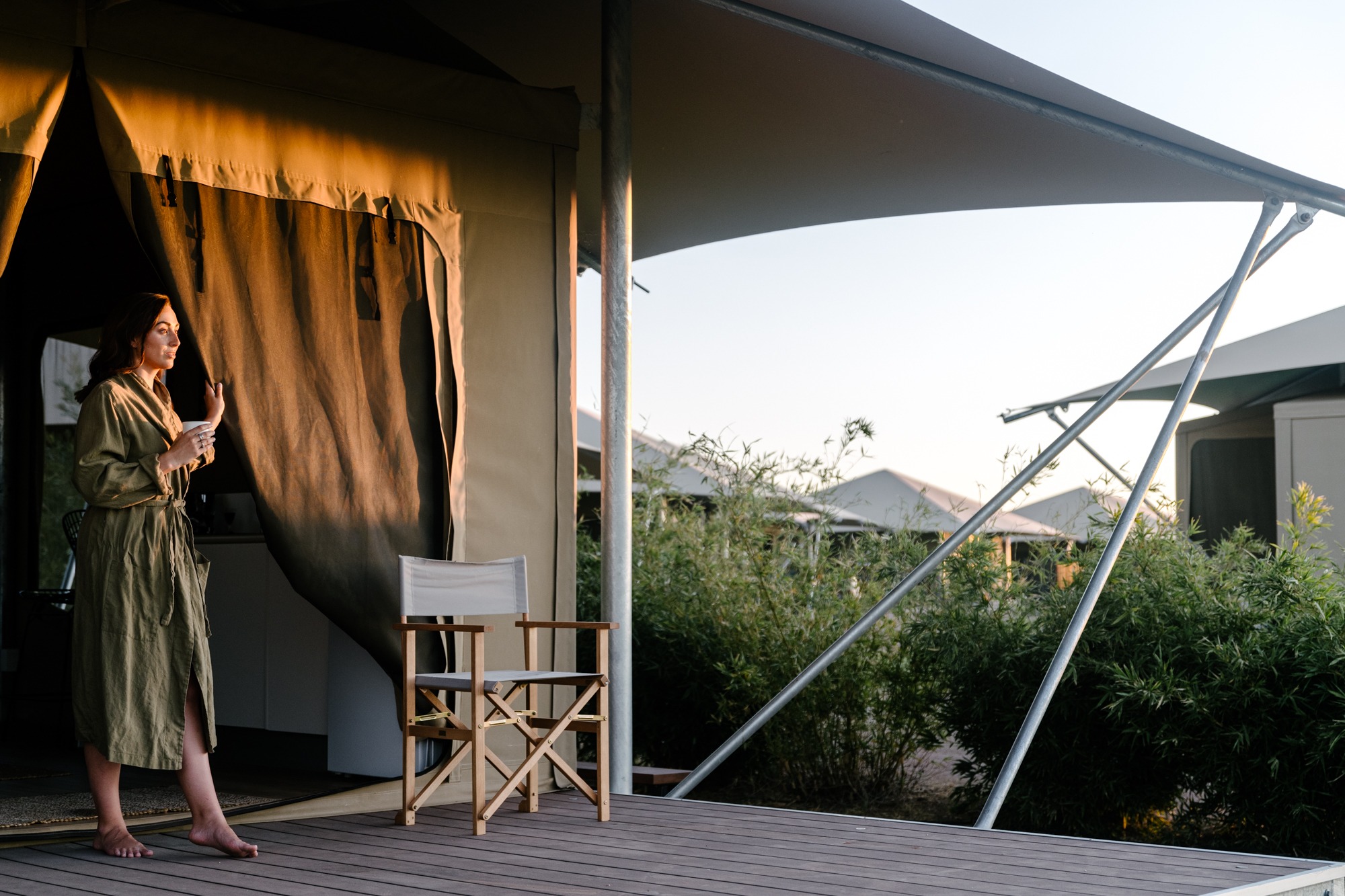 A women in green bathrobe taking in the sunrise from the patio of a Gidyea tent at Mitchell Grass Retreat.